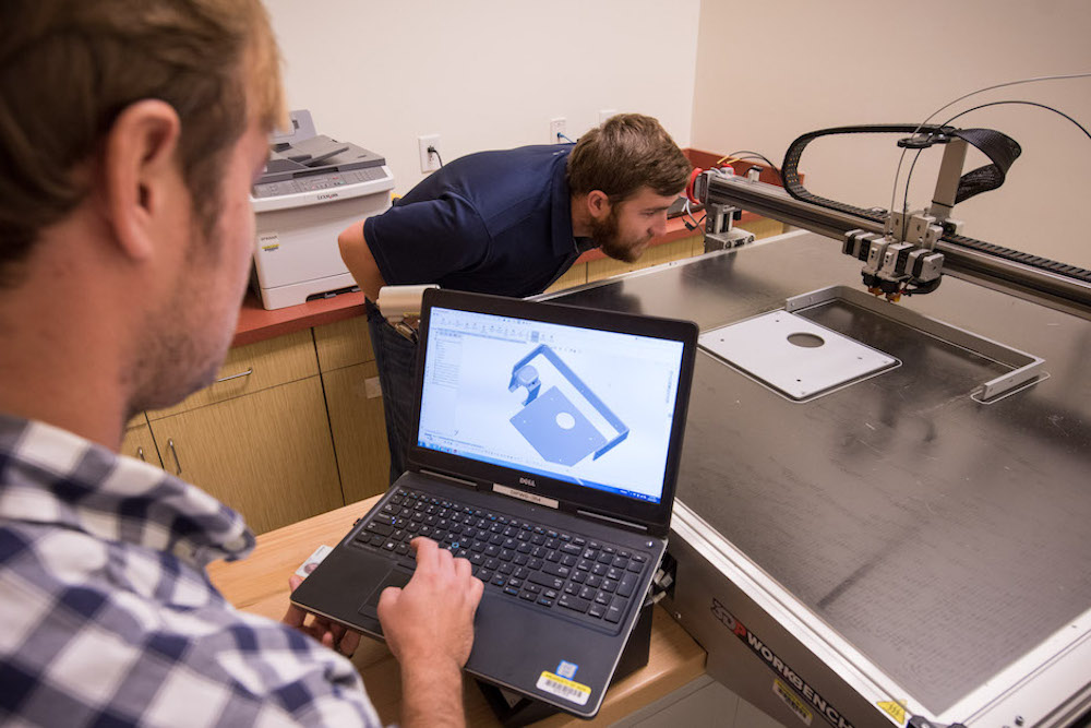 171024-N-GB257-002 Charleston, S.C. (October 24, 2017) SPAWAR Systems Center (SSC) Atlantic employee Josh Heller, left, reviews CAD software designs for additive manufacturing while Ryan Wilhite verifies the printer is properly calibrated. By using Additive Manufacturing technology (aka 3D printing), SSC Atlantic engineers and scientists can design and create prototypes for new components and replacement parts, and enhance and modify existing products. SSC Atlantic develops, acquires and provides life cycle support for command, control, communications, computer, intelligence, surveillance and reconnaissance (C4ISR) systems, information technology and space capabilities. A leading-edge Navy engineering center, SSC Atlantic designs, builds, tests, fields and supports many of the finest frontline C4ISR systems in use today, and those being planned for the future. (U.S. Navy photo by Joe Bullinger/Released)