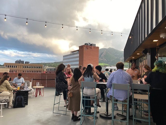 People networking on a rooftop patio with city and mountain views in the background.
