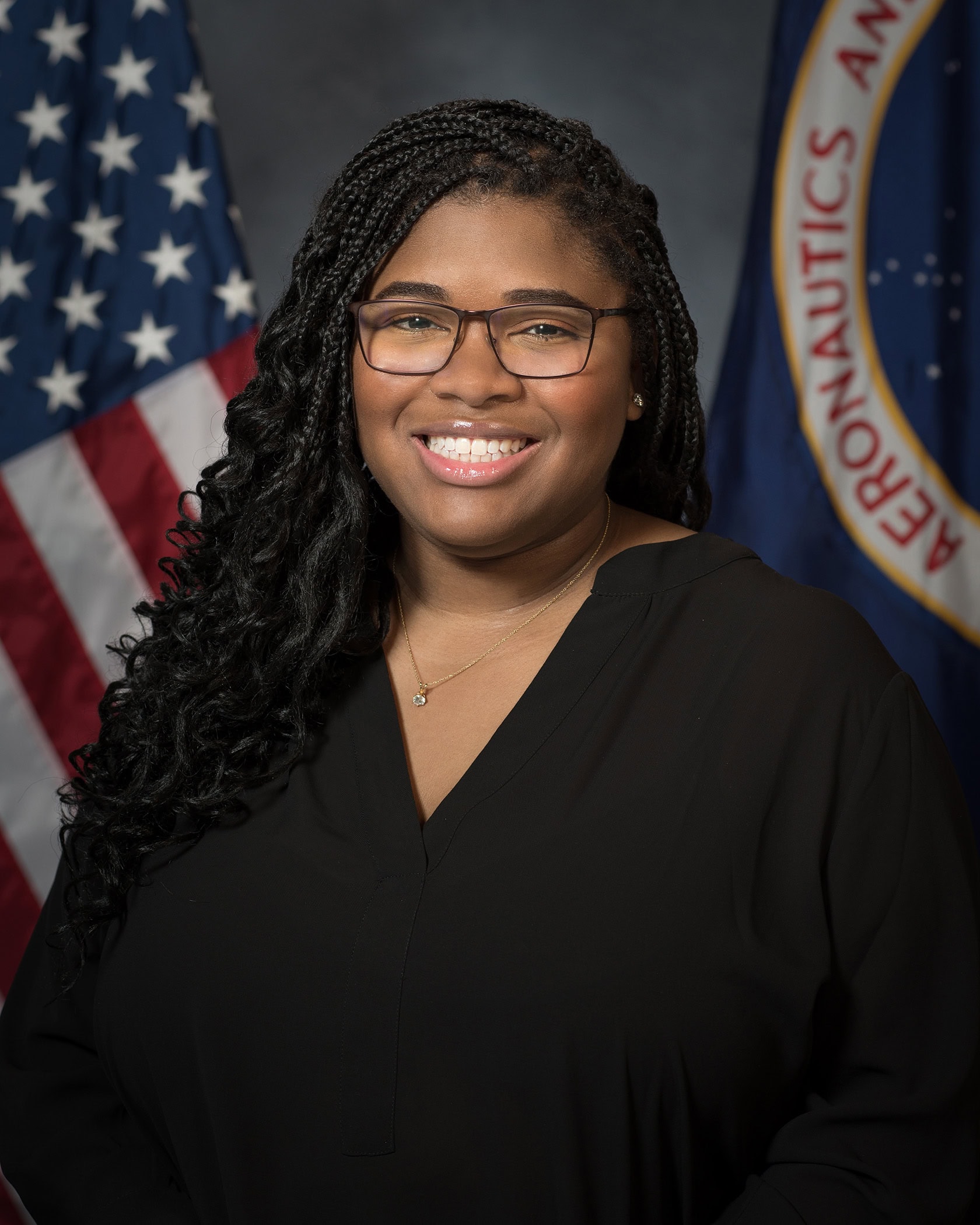 Portrait of a smiling woman with braids wearing glasses, with the US flag and NASA logo in the background.