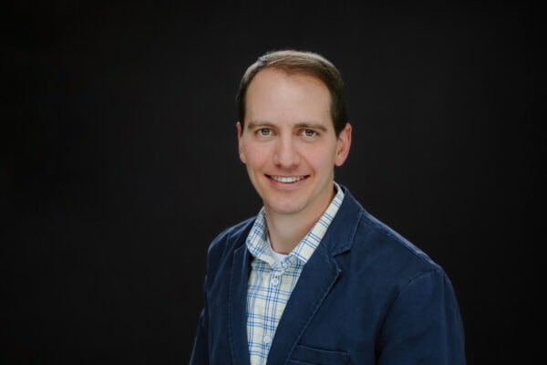 ACNS 2026 speaker: Smiling man in blue jacket and checkered shirt.